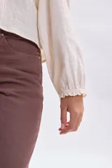 Blusa de estilo romántico en color crudo, confeccionada en tela texturizada con detalles de encaje y alforzas en el canesú. Presenta cuello redondo, cierre frontal con botones y mangas largas con puños delicados.