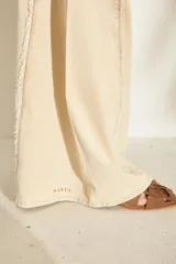 Jeans de corte wide leg, tiro alto y color beige, con detalles de costuras desflecadas a lo largo de las piernas.