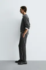 Pantalón de corte slim fit y color negro, confeccionado en tejido elástico. Cuenta con cintura elástica, trabillas, bolsillos frontales y cierre con cremallera y botón.