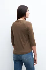 Remera de manga tres cuartos color verde oliva, con cuello redondo y detalles de vainillas (encaje o perforado) en la costura de la sisa.