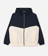 Campera cortavientos deportiva de Ashua, con diseño bicolor en negro y blanco. Presenta capucha integrada ajustable, cierre frontal con cremallera, mangas largas con puños elásticos y cintura elástica. Confeccionada en poliamida con forro de poliéster.