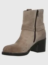 Bota corta de descarne color beige, con taco cuadrado y punta cuadrada. Presenta una correa con argolla metálica decorativa alrededor del tobillo y cierre lateral.