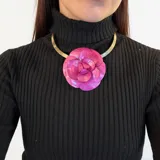 Choker rígido de metal dorado con un dije central grande en forma de flor, elaborado en resina de color fucsia con acabado brillante.