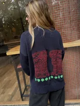 Buzo de punto color azul marino con diseño de conejos bordados a mano en la espalda en tonos rojizos y detalles de puntos verdes en el ruedo. Presenta cuello redondo y mangas largas.
