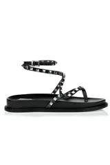 Sandalias planas negras con tiras finas y tobillera ajustable, adornadas con tachas plateadas.