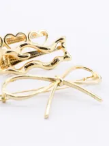 Set de tres broches para el pelo en color dorado. Incluye un broche con tres corazones calados, un broche con diseño ondulado y un broche con forma de lazo.