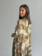 Vestido largo verde con estampado botánico en tonos tostados, escote en V con botones frontales, mangas largas abullonadas y diseño en niveles con volados.