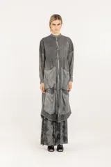Camisa larga de silueta amplia en color gris, con cuello mao y cierre frontal de botones. Presenta hombros caídos, mangas largas semitransparentes, cuatro bolsillos delanteros grandes, ruedo redondeado y pliegue central en la espalda.