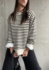 Sweater de punto a rayas horizontales en color natural y negro, con cuello redondo y mangas largas con detalle de botones en los puños.
