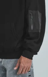 Hoodie oversize de algodón, color negro, con capucha forrada, bolsillo frontal tipo canguro y bolsillo con cierre en la manga estilo bomber.