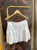 Minifalda blanca acampanada de lino, tiro medio/alto y cierre invisible en la espalda.