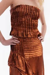 Top strapless de tela metálica con textura plisada, corte ajustado al cuerpo y diseño corto. Incluye una gargantilla a juego del mismo material.