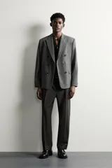 Blazer de corte relaxed fit color gris, confeccionado en tejido con lana. Cuenta con solapas de pico, manga larga con botones en los puños, bolsillos con solapa en la cadera y un bolsillo de vivo en el pecho. Presenta cierre frontal de botonadura cruzada con botones oscuros.