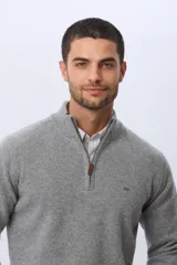 Buzo de tejido de punto color gris, con cuello alto y cierre frontal parcial. Presenta puños y ruedo acanalados, con un pequeño logo bordado en el pecho.