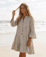 Vestido corto de lino natural color beige, con diseño amplio, cuello mao, cierre frontal parcial con botones de coco, mangas tres cuartos con volados y falda con niveles fruncidos.