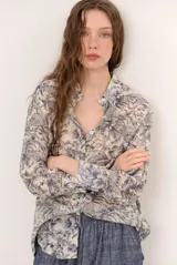 Camisa de seda color celeste y beige, con estampado de hojas en tonos azules, cuello camisero, manga larga y cierre frontal de botones.