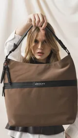 Cartera tipo hobo de tamaño grande en color beige, con detalles en negro. Presenta una franja horizontal negra con el logo de la marca, asa corta de hombro y correa larga desmontable. Incluye bolsillo frontal con cierre oculto y bolsillo trasero.
