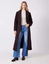 Tapado largo de bouclé color marrón oscuro, con silueta entallada que termina en evasé. Tiene cuello de solapa amplia, cierre frontal con tres botones a tono y bolsillos funcionales con solapa. Incluye forro interno a tono.