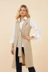 Chaleco largo color marrón claro, abierto, con lazo en la delantera y bolsillos ojal. Confeccionado en lana fina sin teñir.