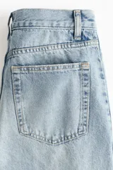 Jean de cinco bolsillos en denim de algodón rígido, con diseño de piernas curvas y volumen, de corte holgado desde la cadera hasta los muslos y ligeramente más ceñido en el bajo. Cintura clásica con cierre de botón y cremallera.