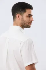 Camisa de manga corta confeccionada en mezcla de lino y algodón, color beige, con cuello camisero abotonado, bolsillo frontal en el pecho y cierre de botones.