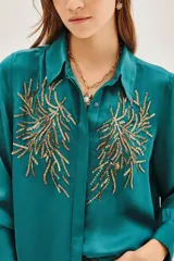 Camisa de viscosa color violeta con cuello clásico, manga larga y cierre frontal con botones. Presenta un diseño bordado con lentejuelas doradas en ambos lados del pecho.