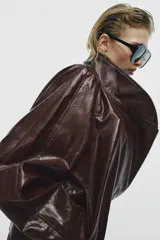 Chaqueta de corte amplio estilo biker en tejido efecto piel de color verde oscuro, con cuello alto envolvente, cierre frontal asimétrico de cremallera metálica, bolsillos ocultos en costura y forro interior.