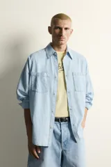Camisa de corte relajado confeccionada en denim ligero de algodón, con cuello solapa, manga larga con puños abotonados y bolsillos de plastrón en el pecho. Presenta un acabado con efecto lavado y cierre frontal mediante botones.