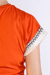 Remera de manga corta color naranja, confeccionada en algodón, con detalles de flecos y bordado en las mangas.
