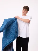 Campera reversible de nylon con cuello alto y cierre frontal. Un lado es de color gris liso con logo bordado, mientras que el otro lado presenta un estampado abstracto en tonos azules. Cuenta con bolsillos laterales y puños elásticos.