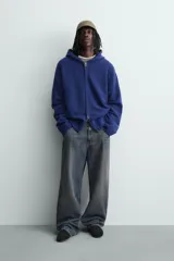 Chaqueta de punto de corte relajado, color azul, con capucha, cierre frontal con cremallera y acabados en rib en puños y bajo.