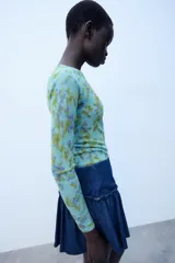 Jersey de punto Zara con cuello redondo y manga larga, con estampado floral a contraste en tonos verdes y morados sobre base celeste.