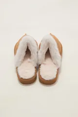 Pantuflas cerradas color marrón con ribetes de piel sintética en la abertura y suela plana.