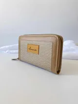 Billetera grande con cierre metálico, color beige. Presenta un panel central con textura tejida o tramada en tono claro y bordes de cuero liso en tono beige más oscuro. Posee un parche de cuero con la palabra "chouie" escrita a mano.
