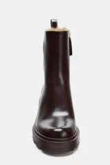 Botín de tacón alto en bloque, color marrón oscuro, con suela track y forro interior de pelo sintético. Presenta pespuntes decorativos, tirador trasero con detalle metálico y cierre mediante cremallera lateral.