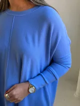 Sweater de punto color celeste, de corte holgado y diseño asimétrico con tajos laterales. Presenta cuello redondo, mangas largas y una costura vertical central en el frente.