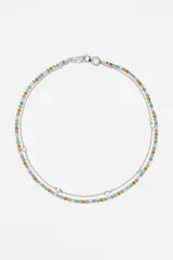 Collar de doble cadena que combina una hilera de cristales facetados en diversos colores (rosa, azul, amarillo, naranja y verde) con una cadena fina plateada adornada con pequeños dijes en forma de corazón. Cuenta con un cierre de mosquetón y un detalle circular con logo.