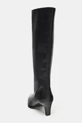 Bota de caña alta confeccionada en piel, con diseño de puntera fina y tacón kitten. Presenta detalle de pespunte en el cuerpo y sistema de calce fácil tipo pull-on.