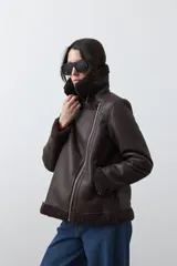 Campera tipo gamulán de símil cuero color marrón oscuro, con interior y solapas de corderito al tono. Presenta cierre frontal cruzado, bolsillos con cierre metálico y hebilla ajustable en el cuello.