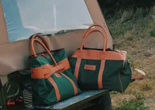 Bolso sport de lona color naranja con detalles y correas en cuero tostado. Cuenta con asas cortas y una correa larga ajustable y desmontable.