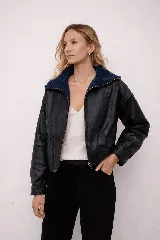Chaqueta estilo bomber de cuero vacuno con diseño bicolor, presentando cuerpo en tono oscuro y cuello de corderito en contraste. Posee cierre frontal completo, mangas largas y corte holgado de inspiración retro.