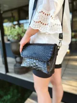 Cartera bandolera de cuero negro con textura tipo cocodrilo, correa larga regulable y forro interno de tela.