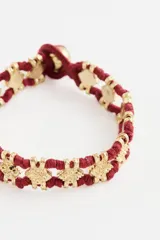 Pulsera de estilo étnico compuesta por cordón de algodón en color rojo y piezas metálicas cuadradas con textura en tono dorado.