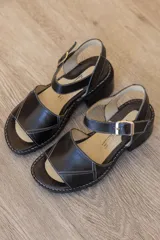 Sandalias de cuero color marrón, con faja frontal ancha con detalle de textura en relieve, plataforma sutil, taco ancho y pulsera ajustable con hebilla en el tobillo.