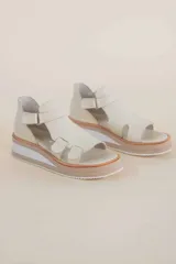 Sandalias de cuero color marfil, con plataforma de 4 cm en tonos beige y blanco, tiras anchas en el empeine con aberturas laterales y tira ajustable en el tobillo con hebilla.