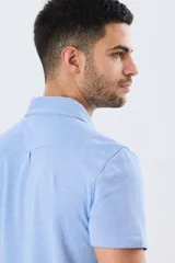 Camisa de piqué lisa color celeste, de manga corta, con cuello camisero y cierre frontal de botones oscuros.