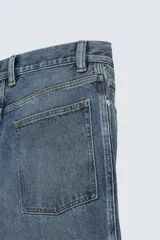 Jeans de corte relaxed fit en denim de algodón, color azul medio lavado. Presenta bordados florales en color blanco o crudo distribuidos en las piernas. Modelo de cinco bolsillos con cierre frontal de cremallera y botón.