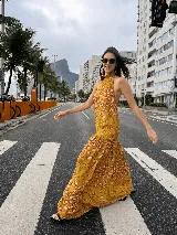Vestido largo de crepe texturado con estampado abstracto de manchas rosadas sobre fondo mostaza, de corte holgado, escote halter con cuello alto con volado y espalda descubierta con cierre de botones.