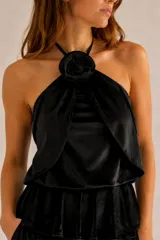 Top negro de terciopelo con cuello halter, diseño holgado y detalle de flor removible en el escote.