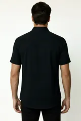 Camisa negra de manga corta, con cuello clásico, cierre frontal con botones y bolsillo ojal en el pecho.